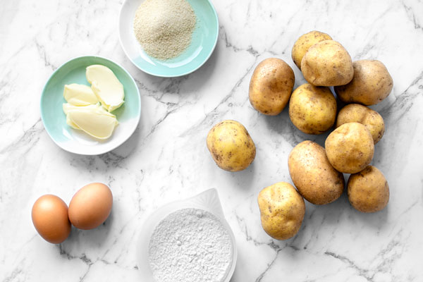 Top view of ingredients for kopytka - Polish Potato Dumplings: Potatoes, Flour, Eggs, and butter with breadcrumbs for a tasty topping.