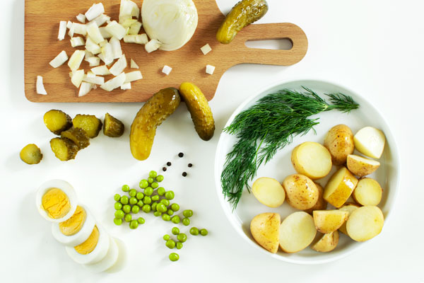 New potatoes, dill, green peas, boiled egg, dill pickle, chopped onion - Ingredients for a potato salad. On a white background, shot from above.