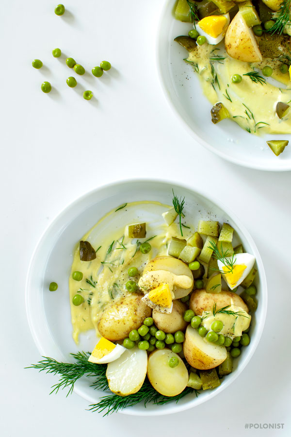 2 white plates with Polish Potato Salad, made with new potatoes, dill pickles, apple, onion, green peas and mayo. On a white background, shot from above.