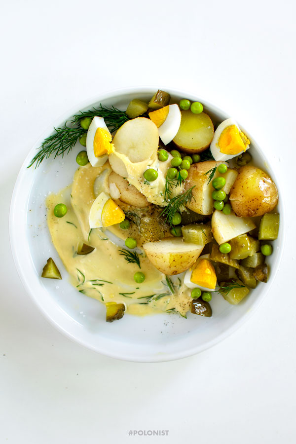 A white plate with Polish Potato Salad, made with new potatoes, dill pickles, apple, onion, green peas and mayo. On a white background, shot from above.