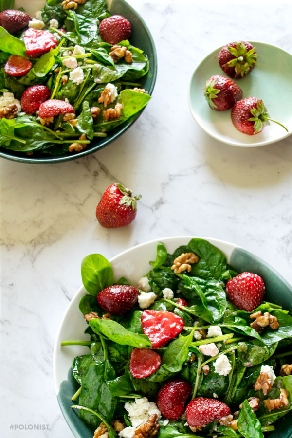 A photograph of two bowls with Baby Spinach Strawberry Walnut Salad with Goat Cheese. On a white marble background.