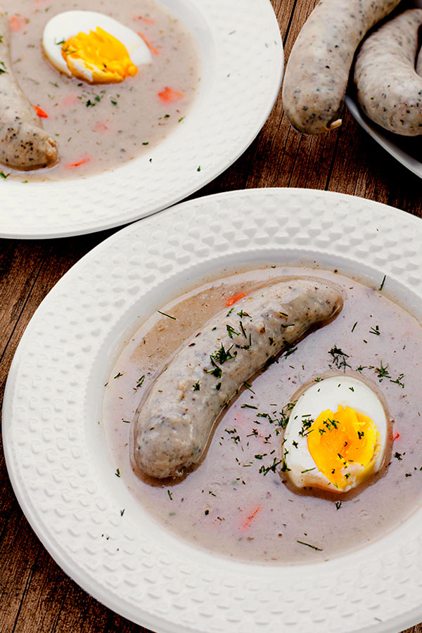 Two plates of White Borscht Soup (Polish Easter Soup) served with boiled egg (halved) and white  kiełbasa sausage 