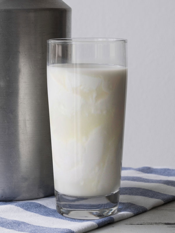 A glass of Soured Milk beside a milk can