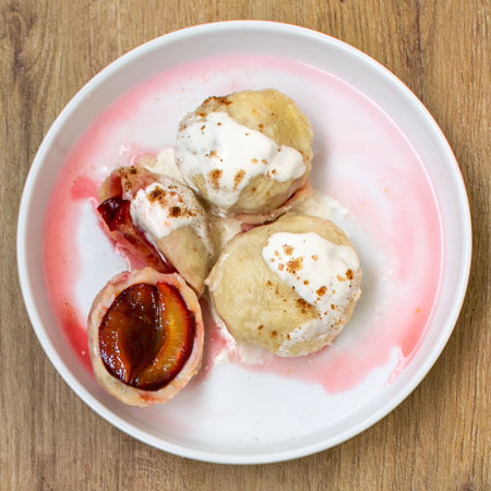 Polish Plum Dumplings "Knedle ze śliwkami" on a white plate, on a wooden table. View from above