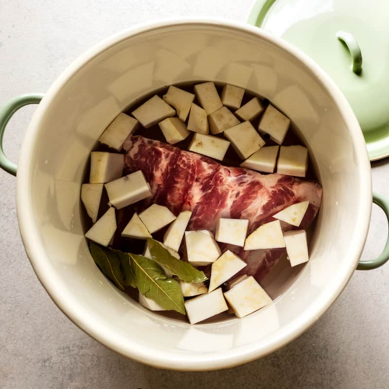 Pot with ingredients for a broth: ribs, celery root, bay leaves